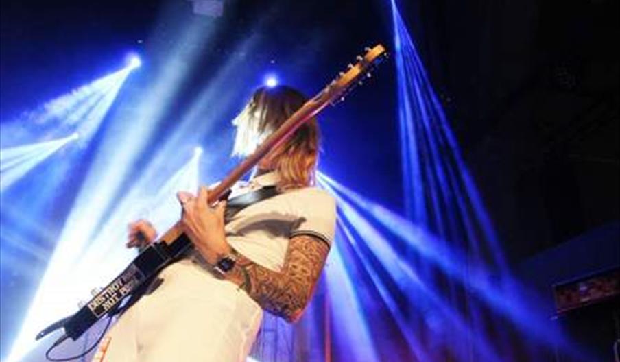 A woman, wearing white, plays electric guitar