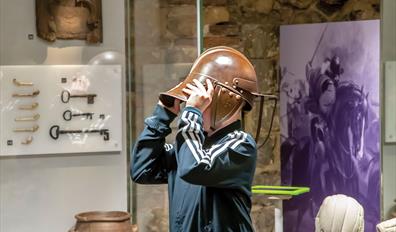 a child trying on a replica roman helmet in a museum