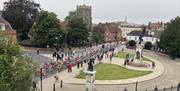 A large group of cyclists race past Colchester's war memorial