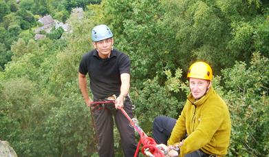 Two men preparing to abseil down rocks into the woods