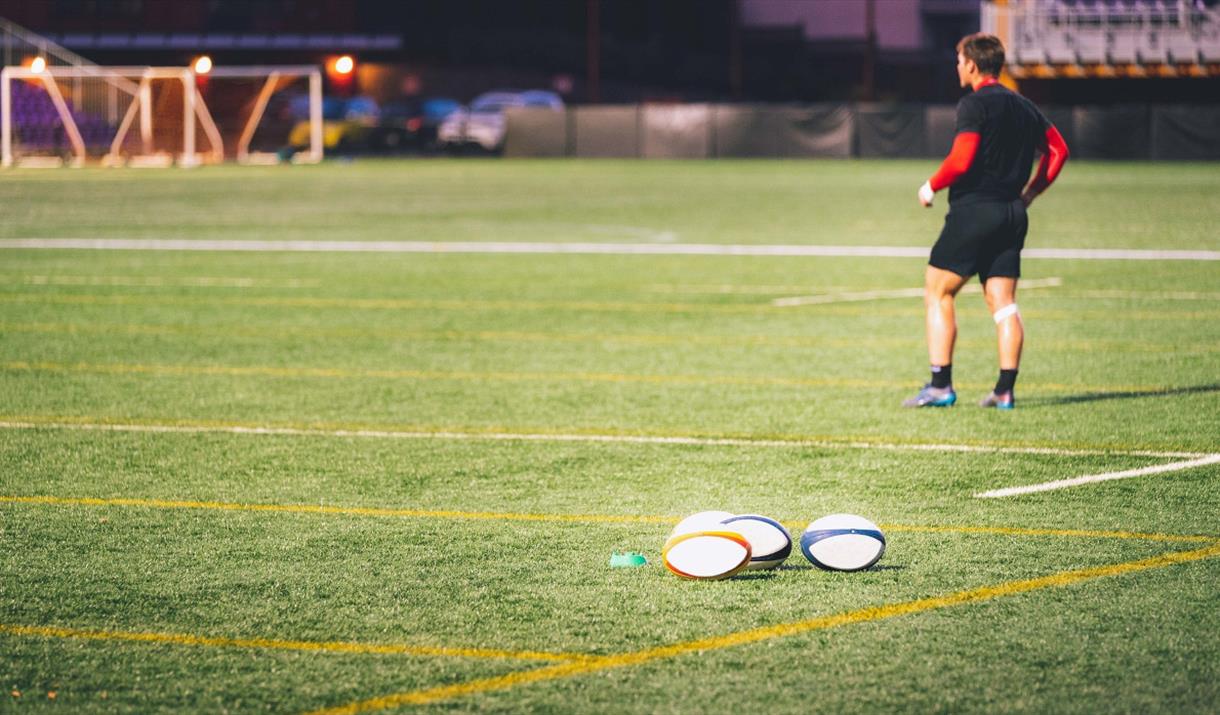 Four rugby balls on the ground with a player in the background
