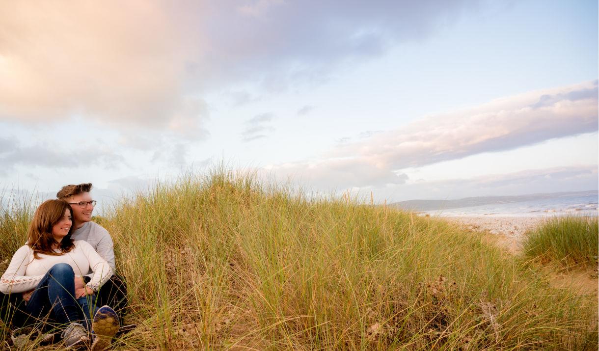 Couple sitting in Kinmel Dunes with sea in background