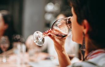 A person drinking from a clear wine glass