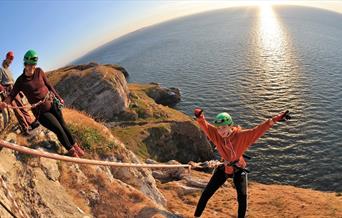 Young child abseiling over cliff edge with ocean in the background