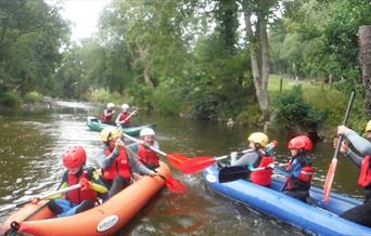 Grwpiau o blant ac oedolion yn mwynhau rafftio ar yr afon