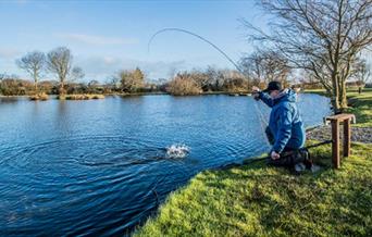 Man casting a fishing rod into trout lake