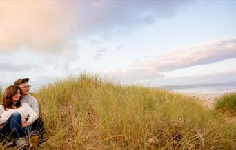 Couple sitting in Kinmel Dunes with sea in background