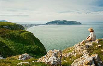 Dyn yn eistedd ar ben Trwyn y Fuwch yn edrych draw i'r Gogarth