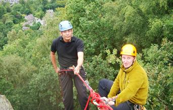 Two men preparing to abseil down rocks into the woods