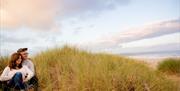 Couple sitting in Kinmel Dunes with sea in background