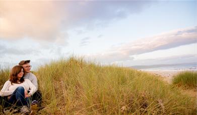 Couple sitting in Kinmel Dunes with sea in background