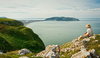 Dyn yn eistedd ar ben Trwyn y Fuwch yn edrych draw i'r Gogarth