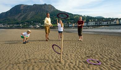 Teulu yn chwarae coets ar Draeth Llanfairfechan