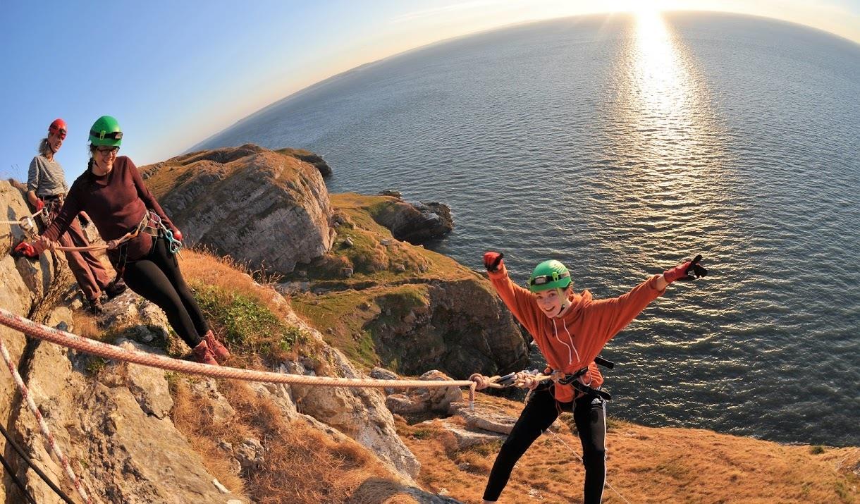 Young child abseiling over cliff edge with ocean in the background