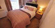 Image of double bed with light pink and white bedding and a heart picture cushion