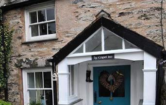 Image of stone cottage with sash windows with a teal front door and heart shaped wreath on the front.
