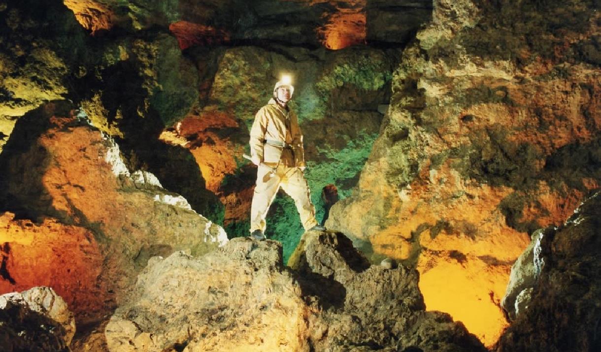 Man standing in a cave with a helmet and light