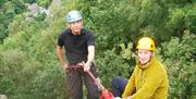 Two men preparing to abseil down rocks into the woods