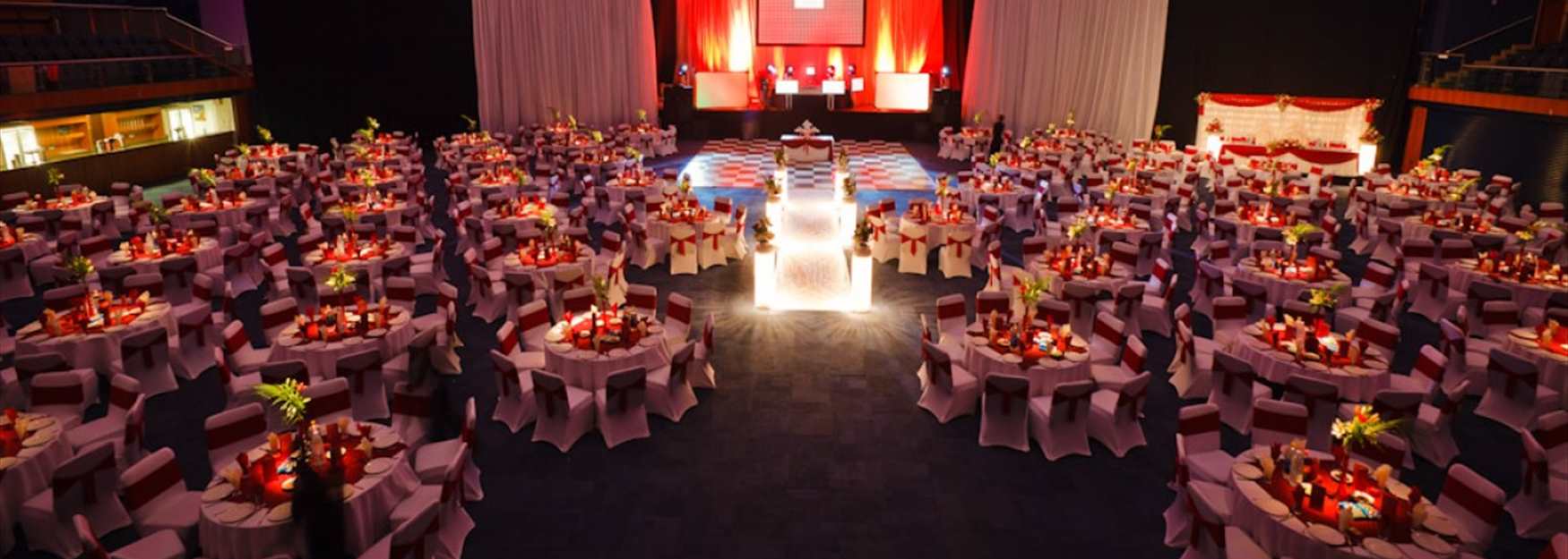 Gala dinner at The Centaur, Cheltenham Racecourse. A stage is set for a band to play behind a chequered dancefloor and round table decorated with flowers