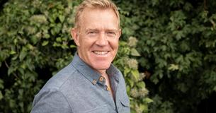 Adam Henson smiling with green hedge behind