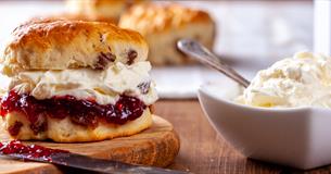 scone filled with jam and cream with a bowl of cream beside it