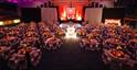 Gala dinner at The Centaur, Cheltenham Racecourse. A stage is set for a band to play behind a chequered dancefloor and round table decorated with flowers