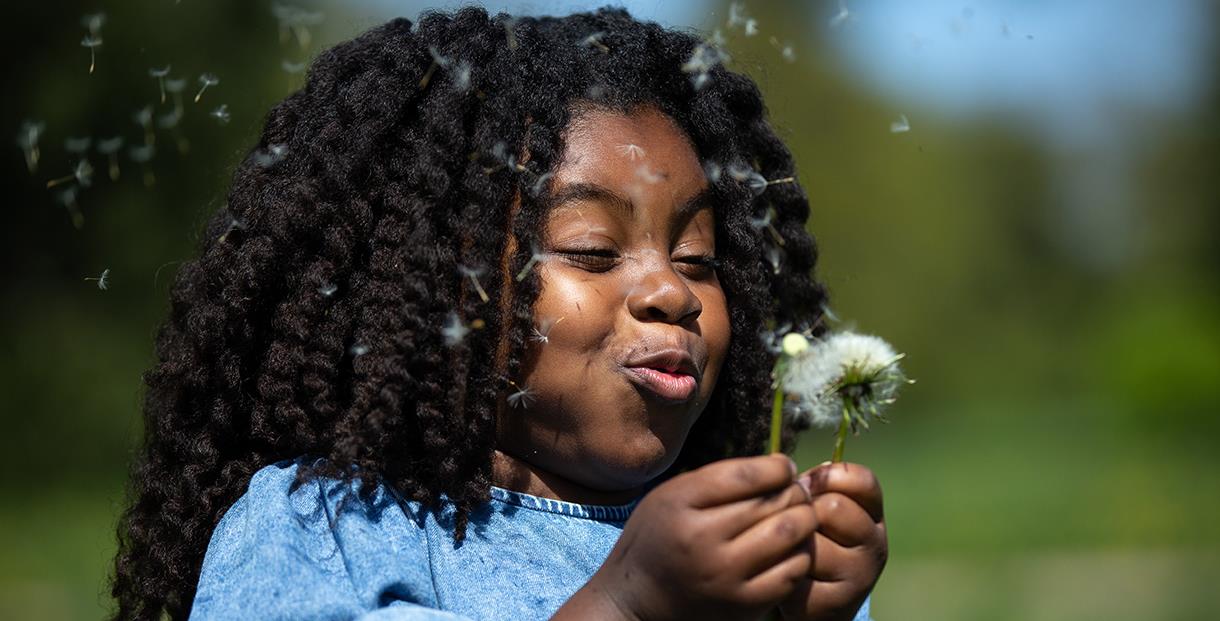 Young girl blowing seeds from dandelion