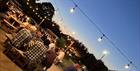 The garden in the evening, filled with people and lit by festoon lights