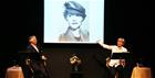 Photo from a performance of Posting Letters to the Moon. Lucy Fleming and her husband Simon Williams sit either side of a stage, a photo from the film