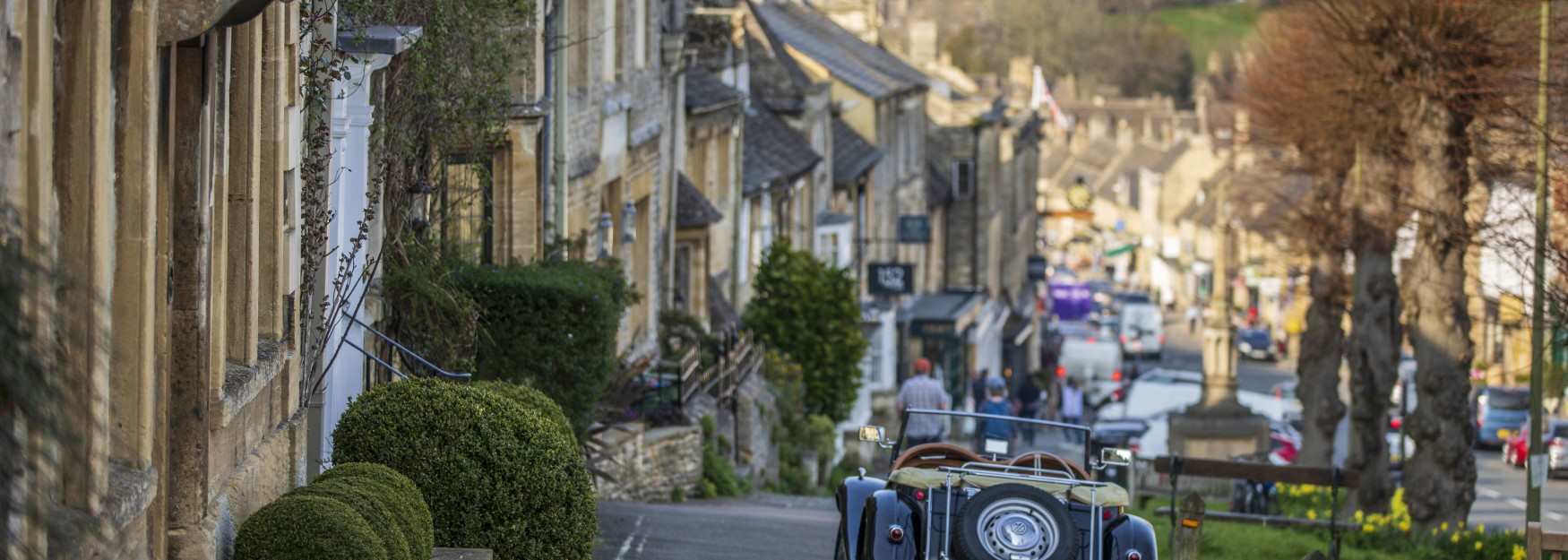 A classic car parked with Burford High Street in the distance