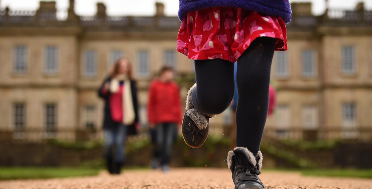 A child running in the grounds with people behind in front of a blurred Dyrham Park house