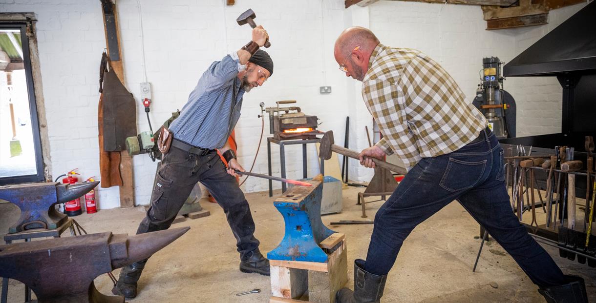 Two blacksmiths working at a forge in a workshop
