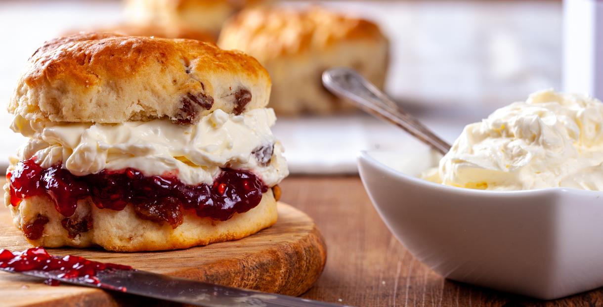 scone filled with jam and cream with a bowl of cream beside it