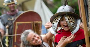 Little boy trying on a gladiator helmet at Chedworth Roman Villa