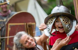Little boy trying on a gladiator helmet at Chedworth Roman Villa