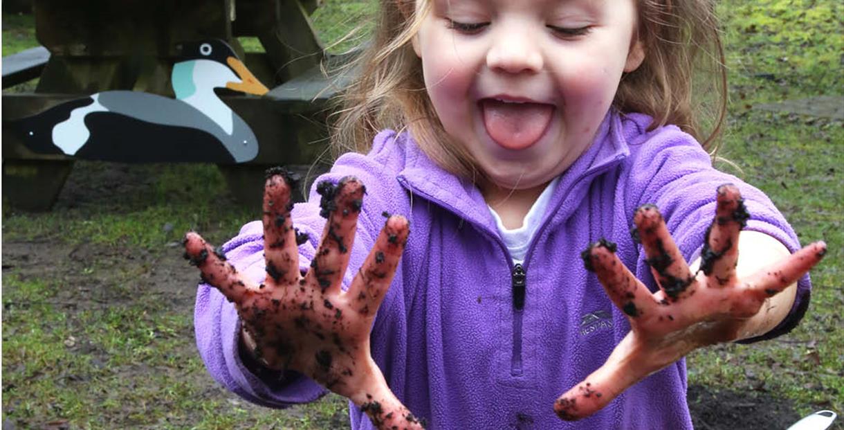 Child holding up muddy hands.