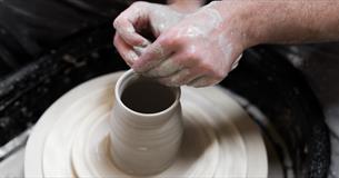 A person throwing a vase on a potters wheel