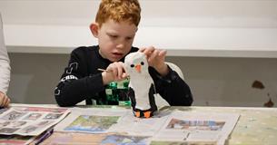 Student painting a penguin sculpture modroc with white, black and orange paint