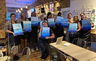 Visitors at a Sip and Paint evening, holding up their artworks