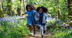 two girls running through spring woodland