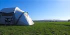 A tent in a field, a blue sky.