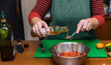 Hands pouring vinegar into a spoon above a mixing bowl full of grated vegetables