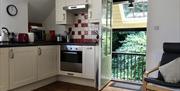 The light and airy living/dining/kitchen area of Granton Coach House, with door to the covered veranda overlooking the patio and small wooded area.