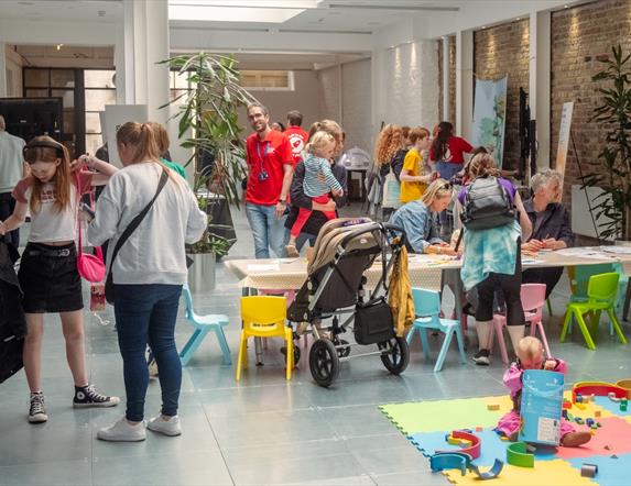 A busy indoor scene  of children and families drawing at a table in a gallery