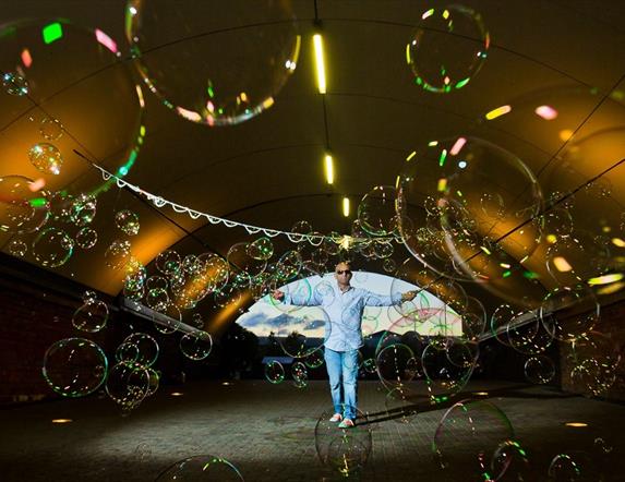 A man in sunglasses stands in a tent surrounded by hundreds of bubbles