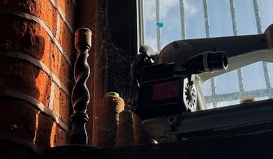A candlestick and old sewing machine on a windowsill covered in cobwebs and dust.