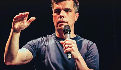 Chris kent holds a mic as he performs his arm slightly bent with his hand raised