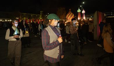 young girl dressed in old style clothing walking with a candle or light.