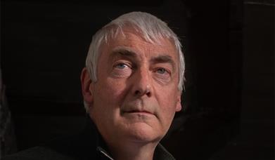 A close-up shot of Kevin McAleer against a black background, gazing vacantly beyond the camera lens.