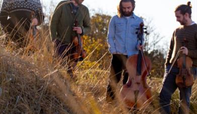 The band made up of 4 gentlemenstand on a hillside holding instruments